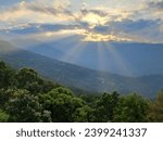 The picture is taken at sunset in the mountains.The rays are coming from behind the clouds. In contrast to the sunrays the greenery below is making a heavenly view.