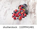 Colorful fresh overhead berries assorted arrangement  in tin metallic can and spilled mixed fruit on rustic white wooden table in studio. Blueberry, raspberry, red currant, strawberry, blackberry