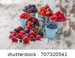 Berries mix blueberry, raspberry, red currant, strawberry, in five old tin cans spilled on white rustic wooden table in studio