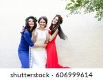 Ladies in blue and red gowns stand around bride posing before white wall