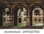 Stone archways leading into a courtyard in Cambridge, UK. Hanging baskets of flowers adorn the brick building.