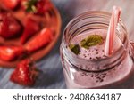 Small photo of Closeup of homemade strawberry milk shake with chia seeds and green mint leaves in a jar with a tubule on a wooden background. Organic vitamin dessert. Top view