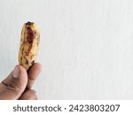 Small photo of Close up of hand holding almost rotten banana with brown and blackish skin texture. Small banana isolated on white background.