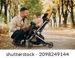 Father with little son walking in baby stroller in autumnal park