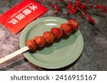 Small photo of A plate of tasty candied haws with four Chinese characters on red paper that translation means "candied haws" and a big characters in the backgroud which means 'happiness' in English.