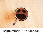 Small photo of Coffee cup with funny scream in fear face, top view. Open cry mouth, eyes in mug on table background. Shocked, stressed, angry, scary and furious foam smile head. Pareidolia effect at breakfast