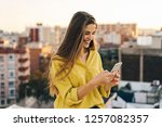 young attractive woman using her smartphone for send a message. female in a yellow blouse smiling on the rooftop while light is magic. Girl checking mobile phone. business woman watching at the screen