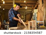 Small photo of Senior carpenter in uniform works on a woodworking machine at the carpentry manufacturing