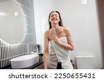 Happy smiling woman having fun, dancing and singing while drying her voluminous hair by hairdryer in bathroom  after morning shower