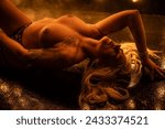 Attractive blonde female posing topless in strapy leather bdsm outfit with whip in front of burlesque light wall with smoke in the air