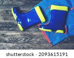 Small photo of Children rain coat and boots. Autumn outfit for kids. Stylish gumboots and coat on wooden background. Blue rain boots and raincoat. Flat lay, top view. Autumn fashion.