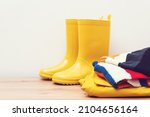 Small photo of Yellow rain boots and outumn outfit. Autumn fashion. Stylish gumboots and coat on wooden shelf. Clothes and boots. Seasonal shopping and sales.
