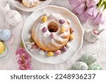 Top view of traditional Easter ring cake sprinkled with powdered sugar and candy eggs on festive table 