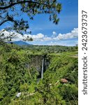 Small photo of Karo Waterfall's enchantment: Cascading waters amidst lush green hills, framed by a canvas of blue sky and clouds, creating a picturesque and serene scene