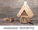 Model of a log cabin next to a magnifying glass, a glass jar of coins and iron key against a wooden background. Business concept. Real estate, business, finance, investment concept. 