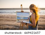 Young woman artist painting landscape in the open air on the beach