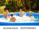 Summer season concept background. Four happy friends are having fun splashing in an inflatable pool in the garden, refreshing themselves in hot weather