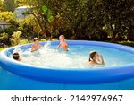 Small photo of Summer season concept background. Four happy friends are having fun splashing in an inflatable pool in the garden, refreshing themselves in hot weather