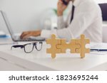 Small photo of Glasses and 3 joined jigsaw puzzle pieces placed on office desk, blurred employee working on laptop computer in background. Concept of effective management, business solutions and finding missing link