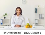 Small photo of Happy smiling dietician sitting at office desk with fresh fruit looking at camera, having individual consultation with client or recording vlog or webinar about weight loss and healthy eating habits