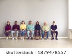 Group of serious diverse people in casual clothes sitting on chairs in row in hospital or company office. Men and women waiting in line for their turn to see a doctor or to have a job interview