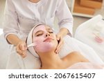 Small photo of Happy calm relaxed beautiful young woman or teenage girl lying on soft towel in beauty parlor or spa salon and enjoying soothing pampering pink kaolin clay facial mask for fresh clear skin, close up