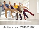 Small photo of Happy dancers posing for a photo standing in a row on one leg. Cheerful friends having fun together during a dancing class. Low angle group shot of smiling young people walking in line in single file