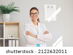 Small photo of Portrait of happy young Caucasian female optician in white medical uniform pose in optics salon. Smiling woman doctor in private clinic or hospital. Eyesight correction. Healthcare, sight problem.