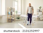 Small photo of Orthopaedic recovery. Man wearing support adjustable fracture fixator on injured leg walks on crutches in hospital office. Concept of rehabilitation of people after serious physical accident injury.