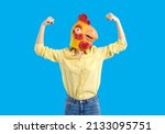 Small photo of Woman in funny chicken disguise pretends to be super strong. Portrait of confident young girl wearing strange weird ridiculous absurd bizarre Hallowen mask flexing her arms isolated on blue background