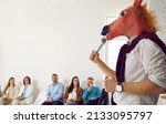 Small photo of Bizarre speaker making funny absurd presentation in front of happy audience. Man wearing silly wacky horse mask holding microphone and giving lecture during business training, conference or seminar