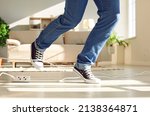 Small photo of Young person trips over an electric cord at home. Close up of a man who's wearing uncomfortable trainers stumbling on a power cable. Close up shot of his feet on the floor. Domestic accident concept