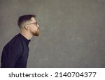 Small photo of Profile side view of young man in glasses pouting lips giving smooch or throwing air kiss at empty grey copy space background. Funny guy with eyes open pretending to make out with imaginary girlfriend