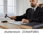 Small photo of Fair serious male judge passes sentence and decides to close case during court hearing. Man in mantle sitting at table pronounces sentence and beats judge's gavel on sound block. Justice concept.