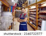 Small photo of Portrait of happy sales assistant at modern DIY store or hardware department at shopping centre. Handsome young man in workwear uniform standing in air vent pipes aisle, looking at camera and smiling