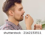 Small photo of Young man takes medication prescribed by his physician. Side profile closeup view of a happy handsome Caucasian man taking a pill and drinking a glass of water. Health, medicine, treatment concept