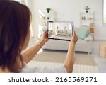Person who plans on selling house or big spacious studio apartment takes photo on tablet device of clean bright Scandinavian Nordic home interior with stylish sofa, shelves, light walls, large windows
