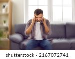 Small photo of Man suddenly feels dizzy and takes a seat on the sofa. Young guy feeling pain and spinning sensation in his head. Headache, vertigo, health problem, brain tumor concept