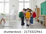 Small photo of Little school friends develop social skills and support each other. Group of elementary students huddling in modern classroom interior . Several children standing in circle and hugging each other