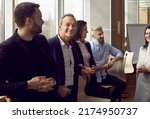 Portrait of senior businessman standing surrounded by his colleagues who are talking in coworking center. Smiling man in suit who is looking camera with confident expression. Business people concept