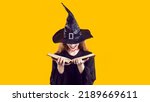 Small photo of Woman in Halloween costume looking through book of spells. Cunning evil witch with bloody neck cut and creepy happy smile hides face under hat and chooses most terrible curse from witchcraft manual