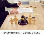 Small photo of Figures of family are separated by judge's gavel, which symbolizes divorce case and custody of child. Close up of wooden figurines of people on background of judges and scales of justice.