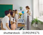 Little grateful children teenagers give bouquet of flowers to woman elementary school tutor as token appreciation or as gift at Teacher Appreciation Week stand in classroom. Education, back to