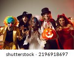 Group of young people dressed up as spooky characters having fun at Halloween costume party. Adult male and female friends with scary makeup on faces doing claw gesture, hissing and making grimaces