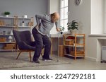 Upset senior man suffering from lower back pain. Elderly man getting up from chair using cane at home. Pensioner having injury and needing rehabilitation. Healthcare and medical concept