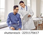 Professional female doctor smiles and shows positive examination results to young, joyful man. Handsome, happy guy with glasses at doctor's appointment in modern office of medical institution.