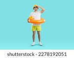 Small photo of Funny joyful young man set up for summer vacation and looking for good offer from travel agency. Happy guy in summer clothes and with inflatable circle looking into distance on light blue background.