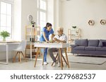 Small photo of Demented senior man spends time in retirement home. Friendly nurse helping old man who is playing games and doing puzzles while sitting at desk in cozy retirement home interior. Dementia care concept