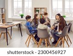 Small photo of Group of elementary school children and their teacher discussing something while sitting in a circle on comfortable chairs in a modern classroom all together