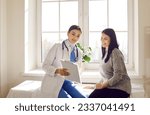 Small photo of Portrait of a young doctor wearing stethoscope holding report file with appointment and giving consultation a smiling woman sitting on the couch in office during medical examination in clinic.